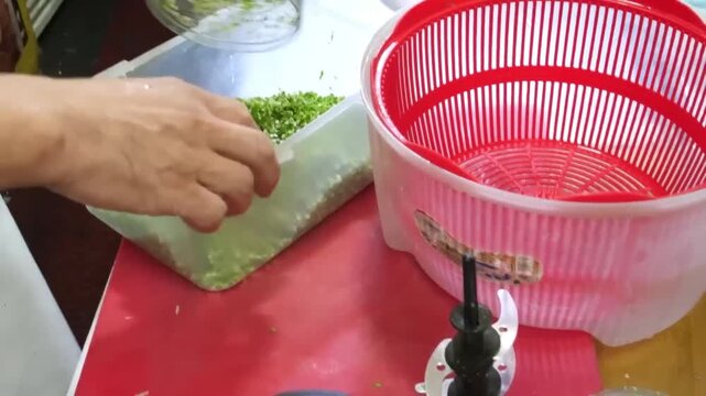 A high-angle, close-up shot showing a hand operating a food processor to grind a mixture of fish, squid, and green herbs to create the base paste for traditional Korean fish cakes, also known as Eomuk