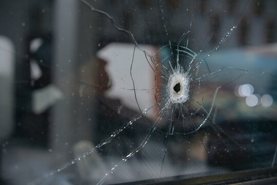 Detailed close up of a bullet hole surrounded by cracked glass on a historic vehicle window. The image highlights impact damage and shattered glass textures.