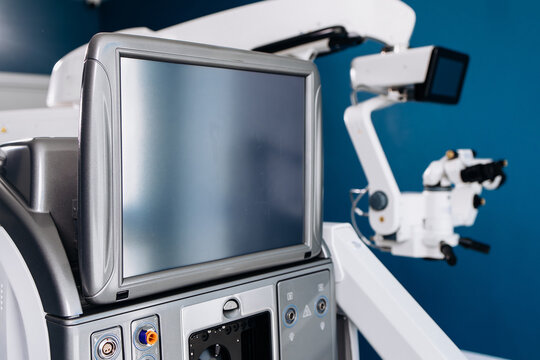 Surgical system for eye operations featuring a control panel and monitor, with advanced optical instruments visible in a clinical setting against a blue wall