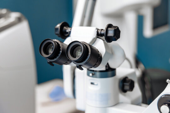 Ophthalmic operating microscope featuring dual eyepieces and precision optics, positioned in a clinical setting with a blurred background of medical equipment