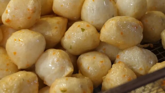 Close-up footage of golden, fried Korean fish cake balls, also known as Eomuk or Odeng. This popular Korean street food is shown with a glistening texture, perfect for travel, culinary, and Asian food