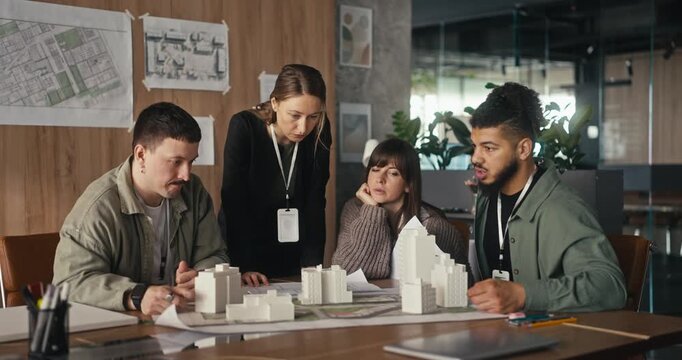 A group discusses and collaborates on a project at a table in an office with models and plans spread out