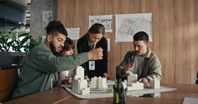 Five people discuss ideas and build a model in a design studio with plans on the walls