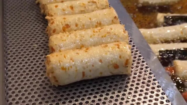 Close-up footage of traditional Korean handmade fish cakes, known as Eomuk or Odeng, being deep-fried in hot oil at a local street food market. The video shows the golden-brown texture of the fish cak
