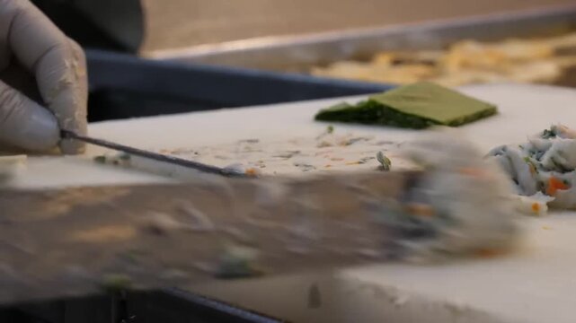 Close-up of a Korean fish cake master expertly shaping fresh seafood paste with chopped vegetables on a white cutting board. The chef uses a specialized metal tool to slice and fold the handmade eomuk