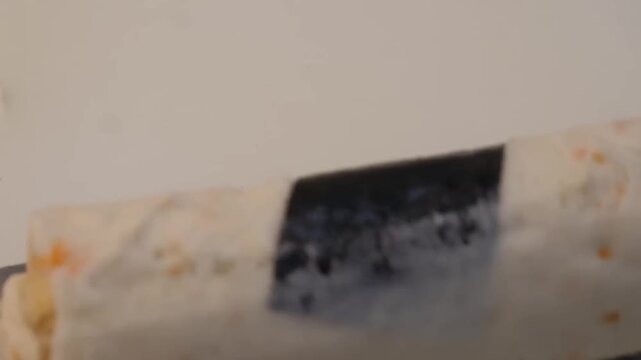 Close-up of a fish cake master shaping traditional Korean eomuk on a professional workspace. The footage captures the process of layering a fresh yellow cheese strip onto a white surimi fish paste ble