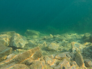 Obraz premium Underwater view of Rummu quarry in Estonia with clear turquoise water and bright sun light reflections on limestone rocks at lake bottom