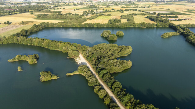Aerial view of Lagoa de Antela, a calm lake with small wooded islands and a narrow dirt path cutting through the water, surrounded by agricultural fields in Ourense, Ourense, Spain.