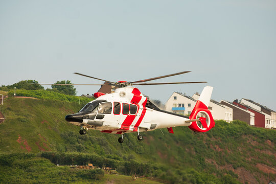 Red and White Rescue Helicopter Flying Over Coastal Hillside Village Buildings, The Concept of Emergency Medical Response