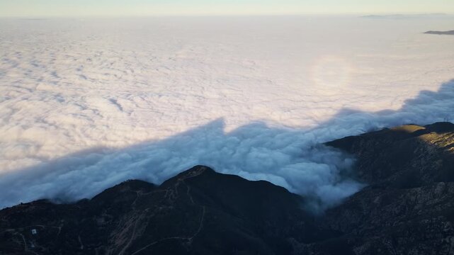 Aerial shot of mountains rising above a layer of low clouds at sunrise. Southern California.