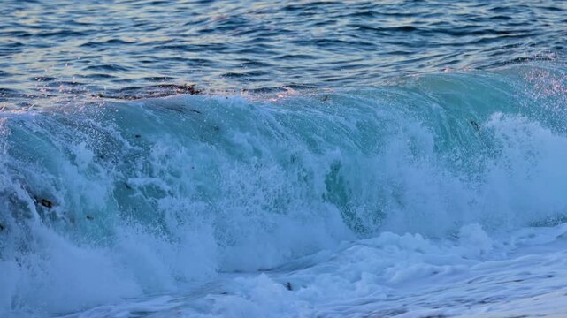 Slow motion shot of ocean wave crashing into a beach at sunset. Shot near Monterey California.