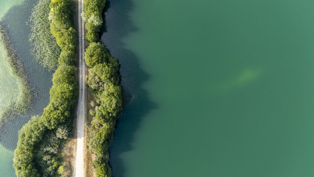 Aerial view of Lagoa da Lontra featuring a narrow path lined with lush green trees bordering the calm turquoise waters of the lake in Sandias, Ourense, Spain.