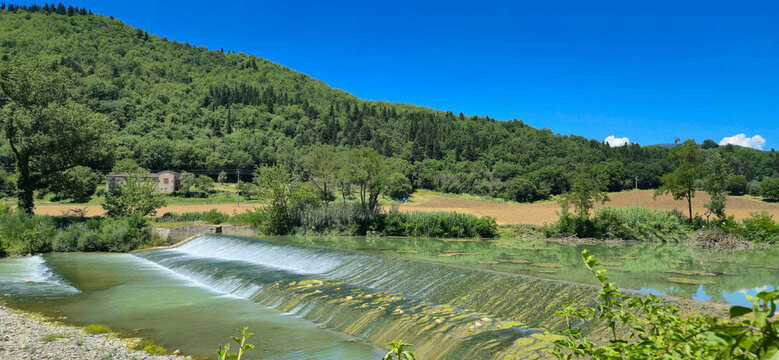 Scenic view of the historic stone weir on the Rufina river in Masseto, Tuscany, Italy. Beautiful countryside landscape with green hills and clear blue sky during summer.