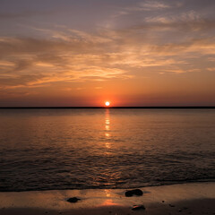 Fototapeta premium Sunset over calm water with distant city lights.