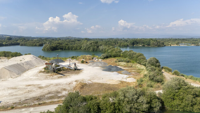 Aerial view of Extraccion de aridos Lima S.L. gravel site with sand piles, machinery, and lake waters in Vilarino das Poldras, Ourense, Spain.