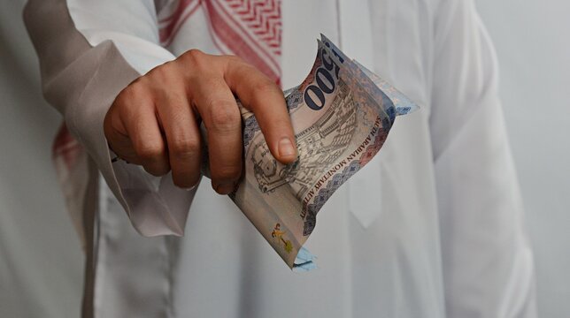 Close up of a Saudi man in traditional clothes counting Saudi Riyal cash notes