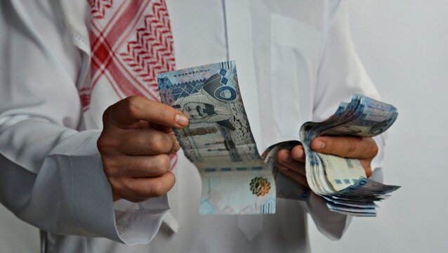 Close up of a Saudi man in traditional clothes counting Saudi Riyal cash notes