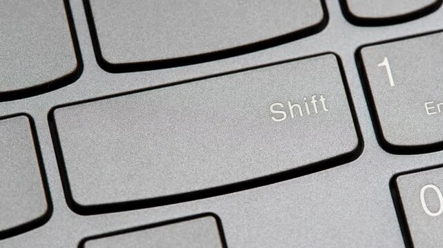 Man pressing the shift key on a modern laptop computer keyboard closeup top view, one person. Shift button key.