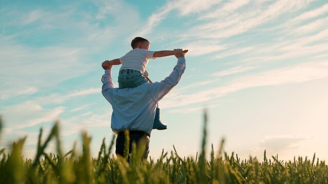 Kid son father play, enjoy nature outdoor, dream of flying, super hero. Family, dad kid with child on their shoulders run through wheat field. Child dreams of fly. Dad, boy child walk together, sky