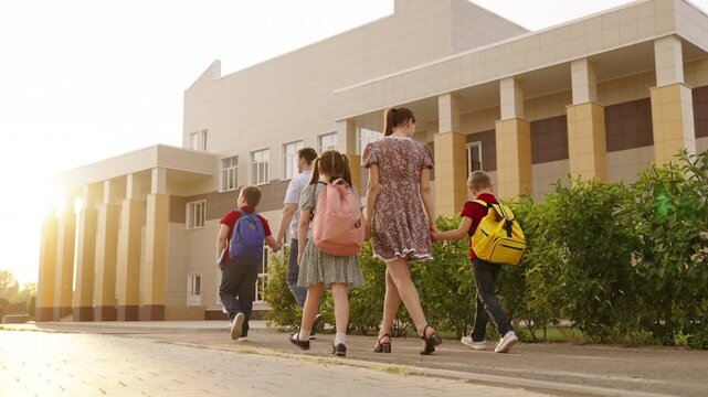 Children walking to school building, Family taking kids to first day of school, Group of students with backpacks outside school, Parents escorting children to educational institution, Kids heading for