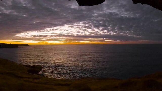 Time lapse video of a sunrise over the ocean viewed through a natural sea cave opening along the Sydney coastline, Australia.