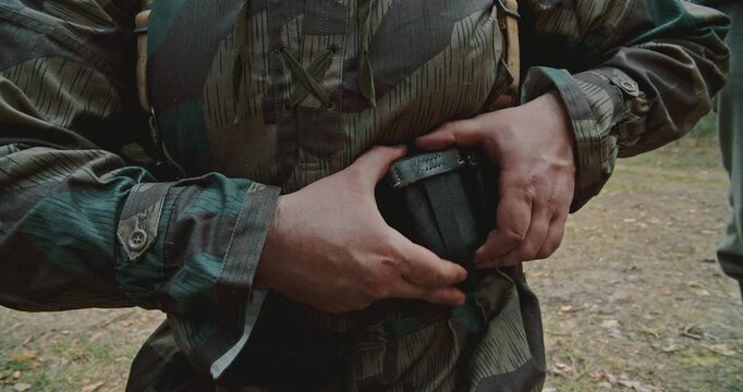 WWII German soldier reaching into leather ammunition pouch on belt
