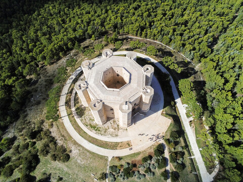 Aerial view of the historic octagonal Castel del Monte surrounded by dense forest and stone pathways in Castel del Monte, Abruzzo, Italy.