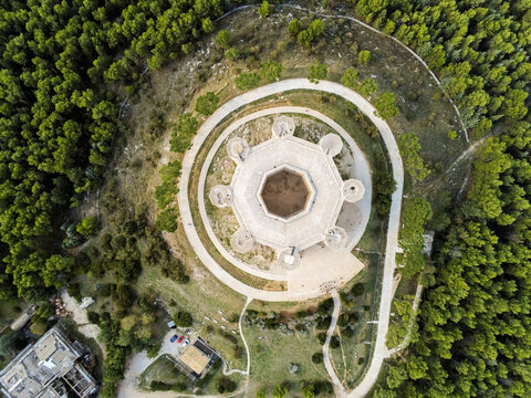 Aerial view of Castel del Monte, a historic 13th-century octagonal castle surrounded by dense pine forests in the Apennine Mountains, Castel del Monte, Abruzzo, Italy.