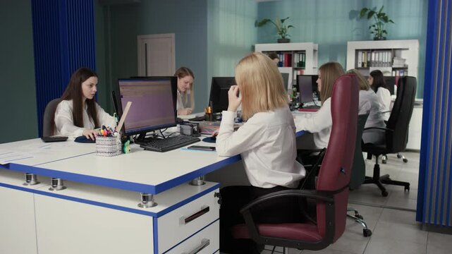 Cinematic footage of several Caucasian women working on their computers in a modern office with blue elements. 4K video.