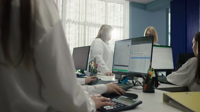 Filming of a data entry process into a computer in a modern office. In the background of the monitor, other women are observed chatting. 4K video.