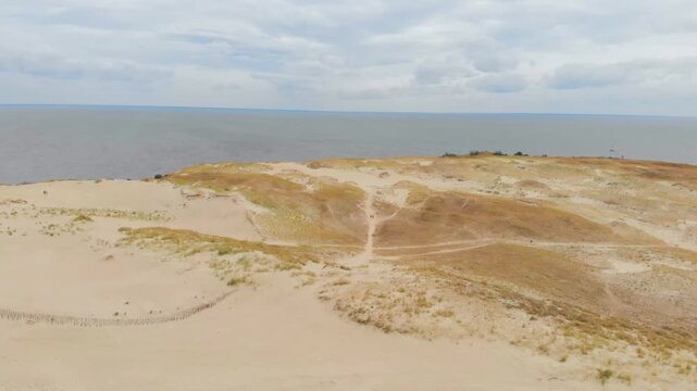 Aerial panoramic view of the vast sand dunes of the Curonian Spit, a UNESCO World Heritage Site in Nida, Lithuania. The landscape features large, rolling sand dunes with sparse vegetation, leading tow