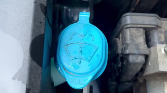 Hand closing blue windshield washer fluid cap inside engine