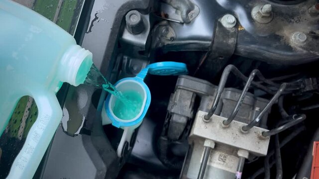 Refilling green washer fluid inside open car engine compartment