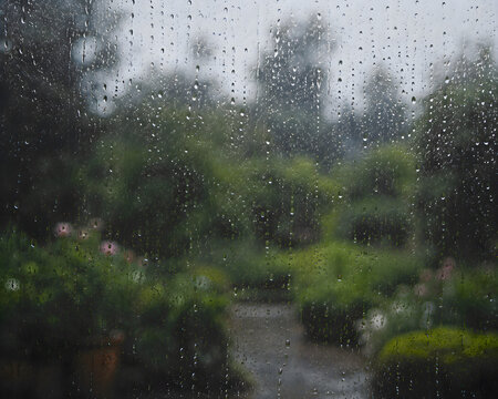 View of a garden through a rain soaked window, wet glass with water drops autumn storm seasonal atmospheric weather landscape portrait asset