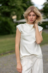 Fototapeta premium Woman stands on pathway in the park wearing light outfit and touching her hair during daytime