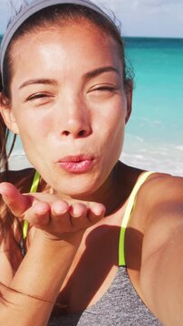 Fitness girl using smart phone on beach blowing kiss having fun on beach vacation during summer travel holidays taking a selfie photo or having video chat. Sexy young bikini woman posing for camera.