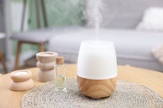 Aromatherapy. Modern aroma lamp, scented candles and bottle of essential oil on table indoors