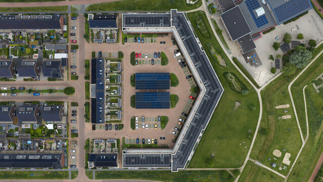Aerial drone view of a solar carport in a modern residential neighborhood, showing renewable energy, covered parking and sustainable living infrastructure.