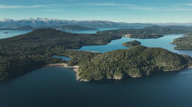 Drone perspective capturing the vast blue waters of Nahuel Huapi Lake surrounded by forested islands and snow-capped Andean peaks in Bariloche, Argentina