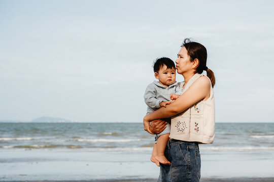 Young mother holding her adorable baby boy travel on the beach at sunny day.
