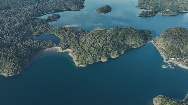 Aerial view showcasing the calm blue waters, islands, and dense shoreline vegetation of Nahuel Huapi Lake. Bariloche