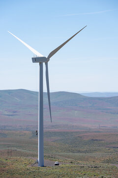 Wind turbine with work truck parked at the base, pully line with work bags attached being pulled up to nacelle on top, dry arid environment
