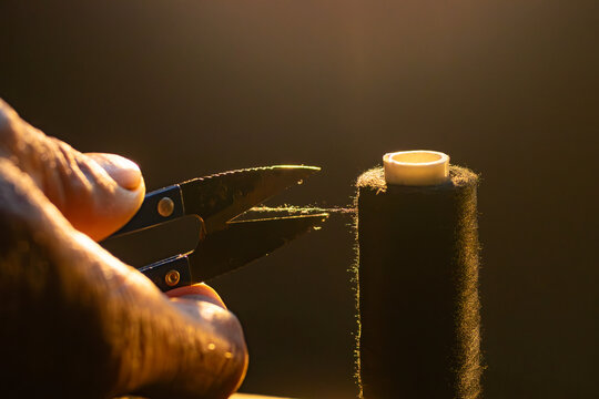 Close up of a tailor hand using small sewing snips to cut a black thread against warm backlit rim light