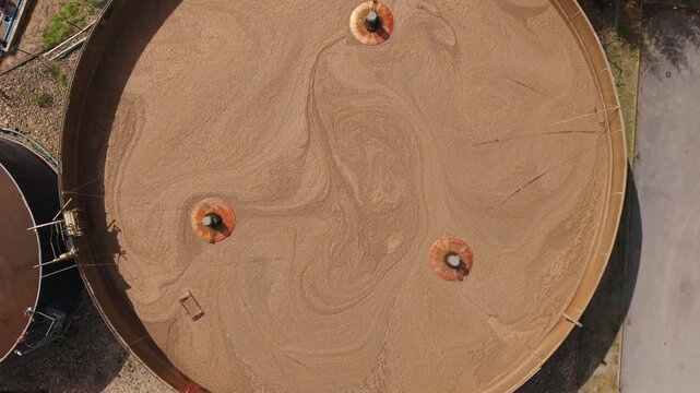 Aerial perspective of expansive circular sand filtration tanks with rotating arms actively stirring sand, illustrating the ongoing process of sand movement and water treatment in an industrial setting