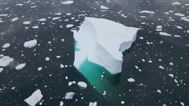 Aerial view of a large iceberg floating in the dark waters of the Ilulissat Icefjord surrounded by smaller ice fragments in Ilulissat, Avannaata Municipalit, Greenland.