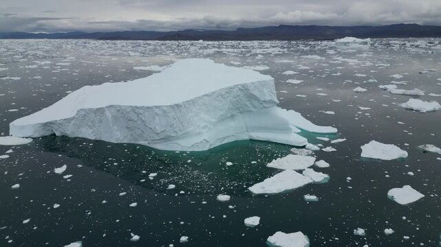 Aerial view of large iceberg floating in the dark waters surrounded by scattered ice fragments in Ilulissat, Avannaata, Greenland.