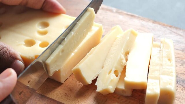 Close up of chef hand slicing yellow swiss cheese with holes on wooden cutting board in kitchen