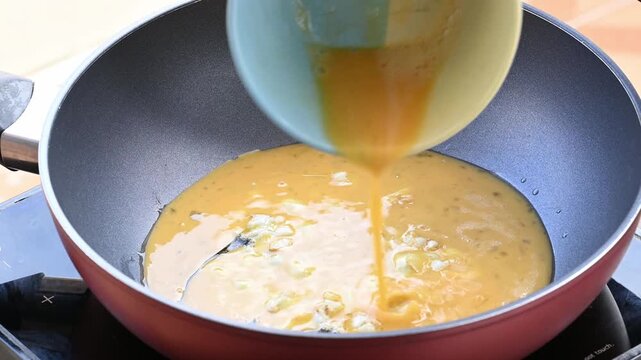 Close up pouring beaten eggs into a hot pan with minced garlic and cooking oil, homemade Asian food 