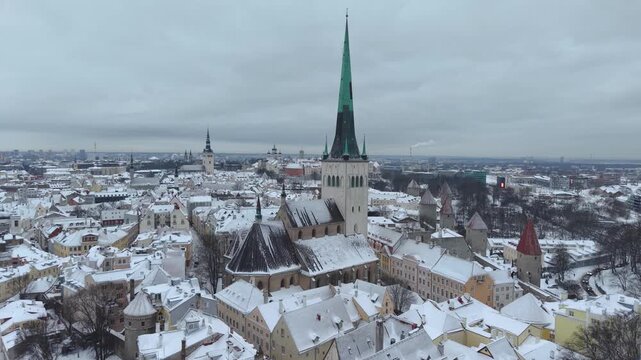 Aerial view of St. Olaf's Church surrounded by historic rooftops covered in snow in the old town of Tallinn, Harju County, Estonia.