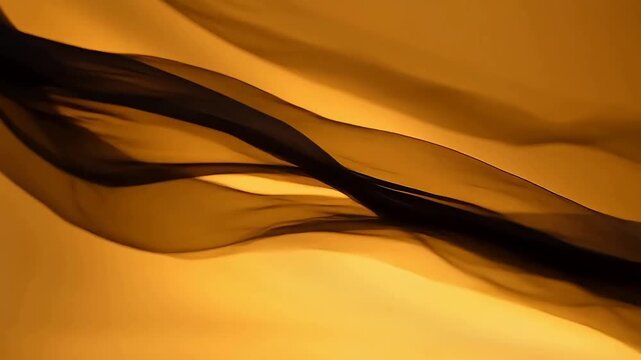 Black sheer fabric flowing gracefully against a warm golden background
